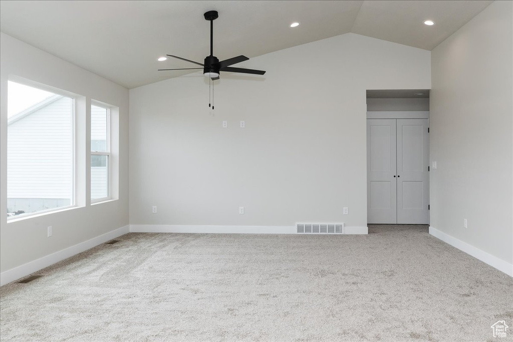 Carpeted spare room featuring baseboards, visible vents, lofted ceiling, and a ceiling fan