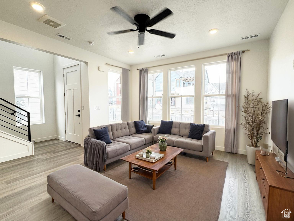 Living area with ceiling fan, visible vents, stairway, and light wood finished floors