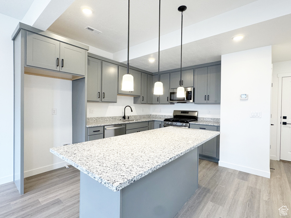 Kitchen featuring visible vents, light wood finished floors, stainless steel appliances, a kitchen island, and gray cabinets
