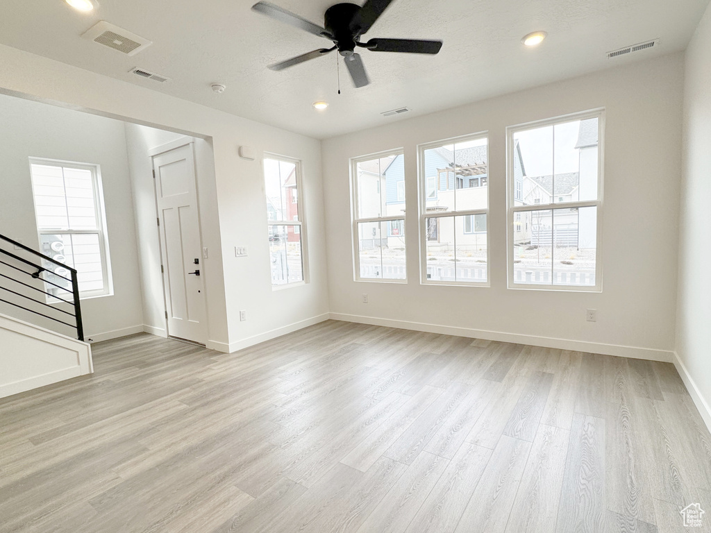 Unfurnished living room featuring stairs, a ceiling fan, baseboards, visible vents, and light wood-style floors