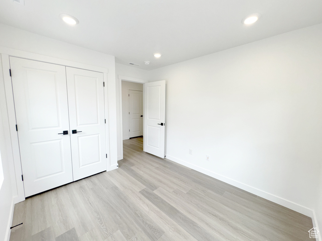 Unfurnished bedroom with baseboards, a closet, light wood-style flooring, and recessed lighting