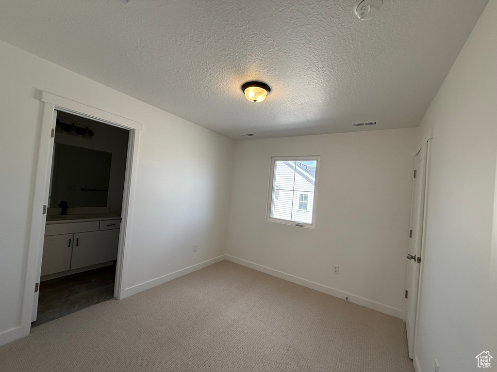 Unfurnished bedroom with a textured ceiling, baseboards, light carpet, and visible vents
