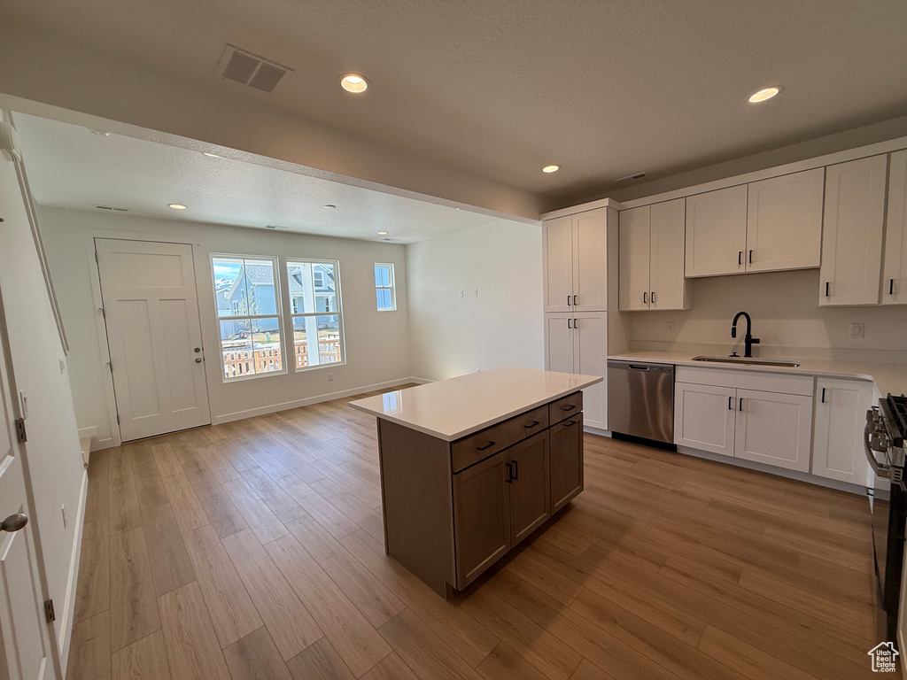 Kitchen featuring light wood-type flooring, light countertops, visible vents, stainless steel dishwasher, and a sink