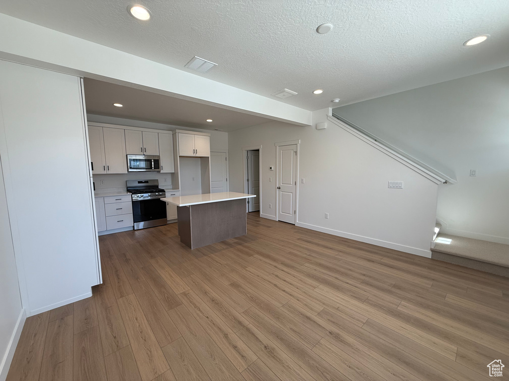 Kitchen featuring baseboards, open floor plan, white cabinets, stainless steel appliances, and light wood finished floors