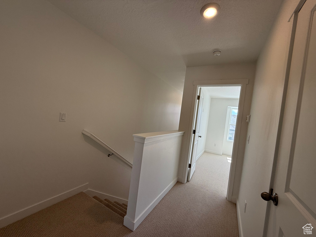 Corridor featuring baseboards, an upstairs landing, light carpet, and a textured ceiling