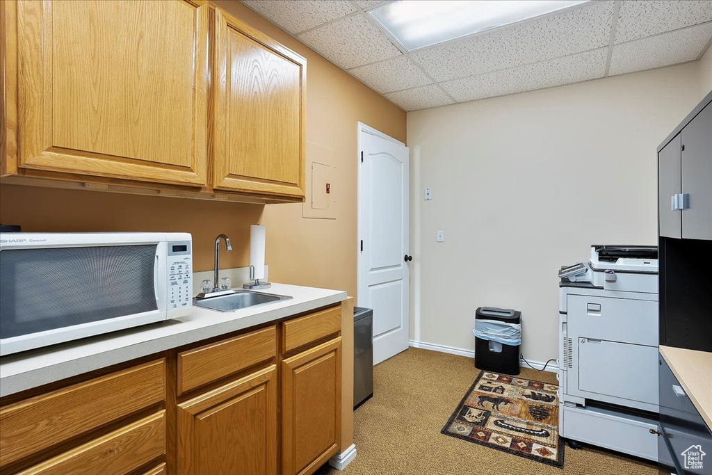 Kitchen featuring light countertops, a sink, a drop ceiling, white microwave, and light colored carpet