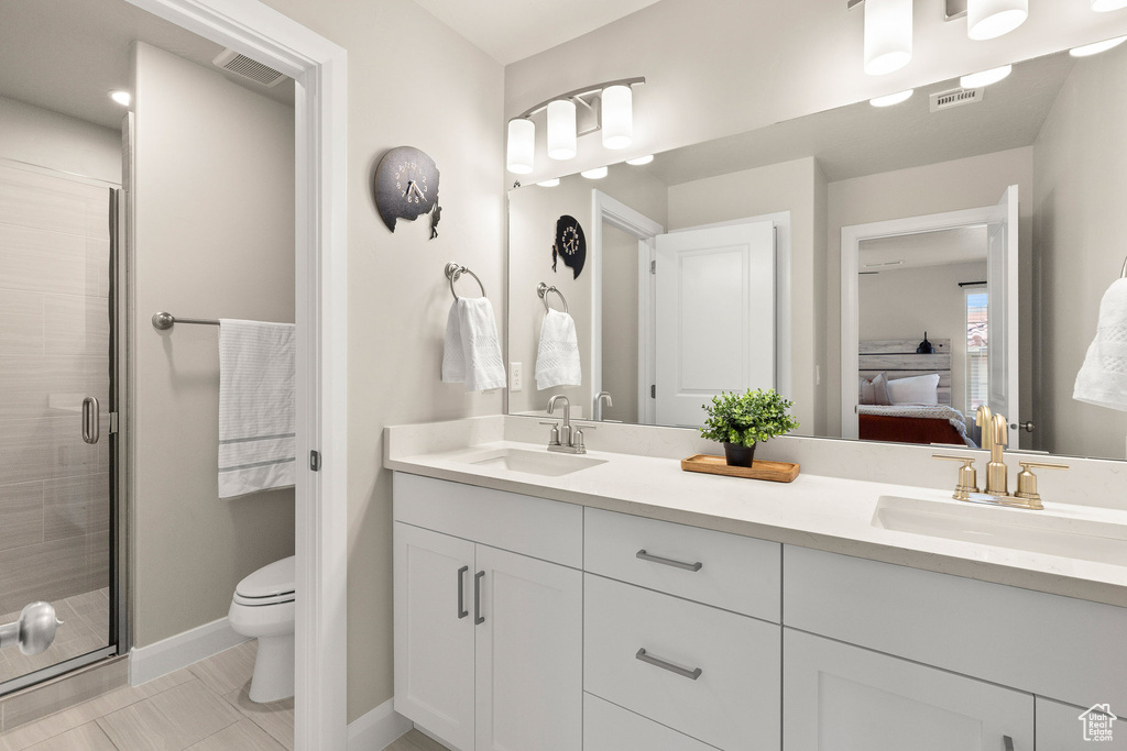 Ensuite bathroom featuring double vanity, a shower stall, toilet, and baseboards