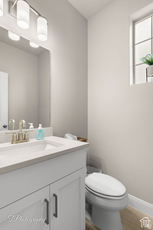 Bathroom with toilet, vanity, wood finished floors, and baseboards