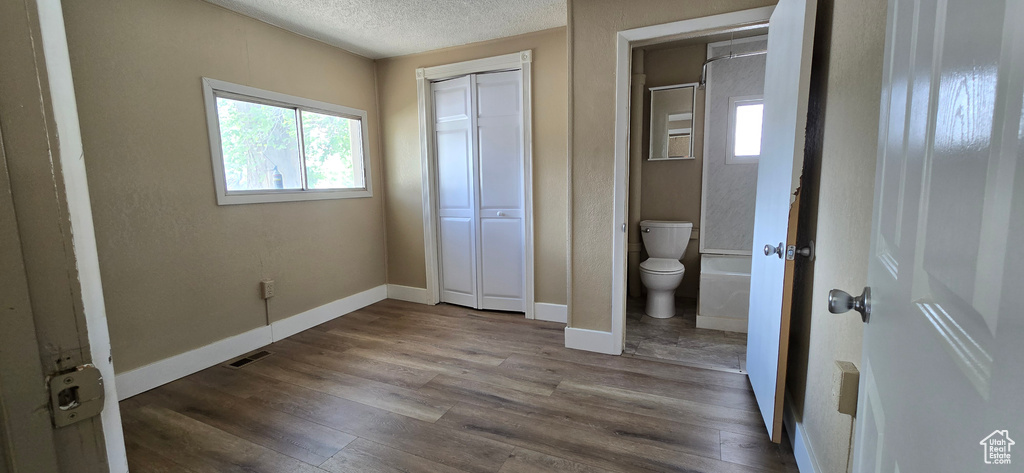 Unfurnished bedroom featuring a textured ceiling, wood finished floors, baseboards, and a closet