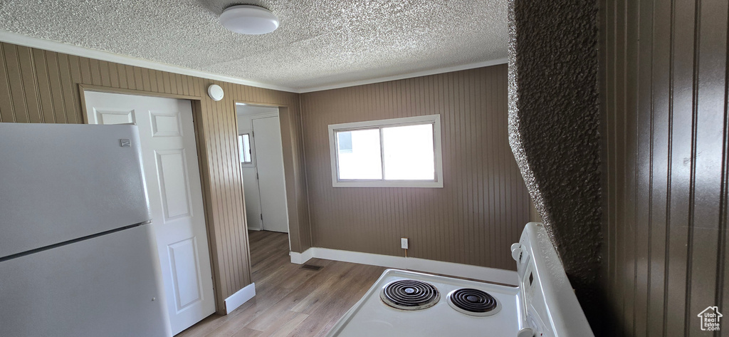 Laundry area featuring ornamental molding, light wood-type flooring, baseboards, and a textured ceiling