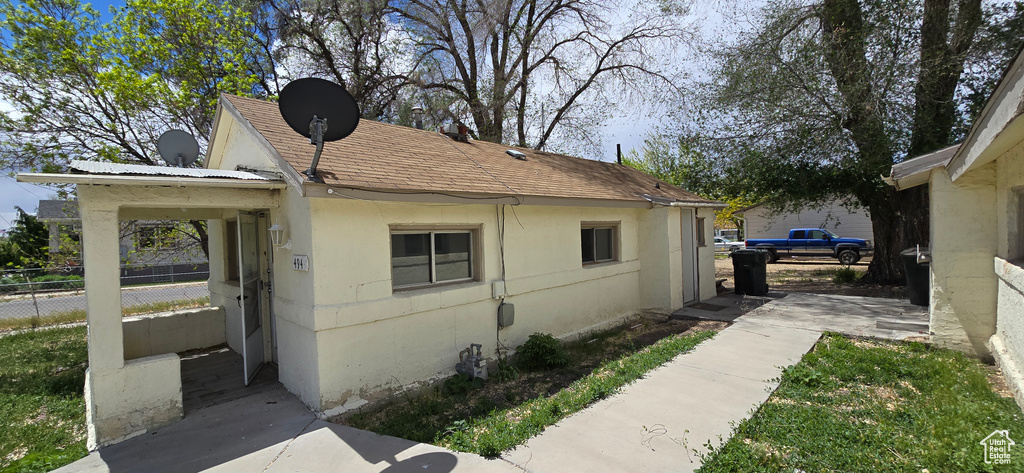 View of side of home with fence, a shingled roof, and stucco siding