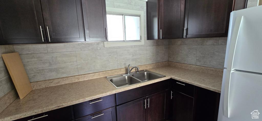 Kitchen with freestanding refrigerator, a sink, backsplash, light countertops, and dark brown cabinetry
