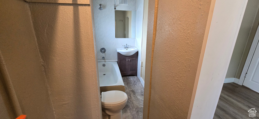 Full bathroom featuring a textured wall, a bath, wood finished floors, toilet, and vanity