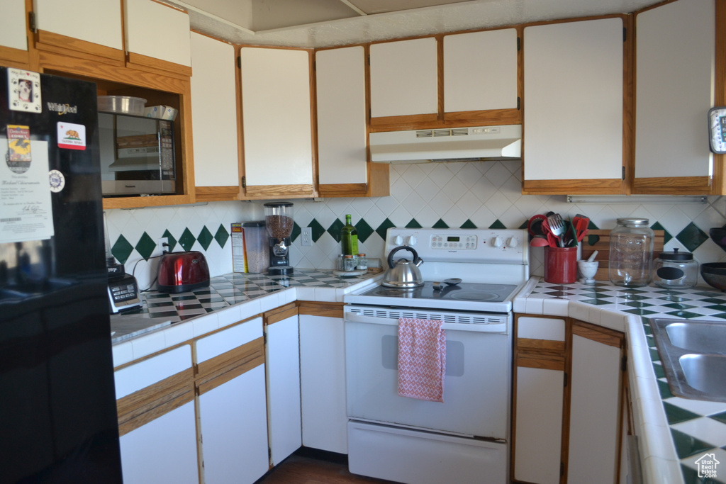 Kitchen featuring white electric range oven, tile counters, stainless steel microwave, under cabinet range hood, and freestanding refrigerator