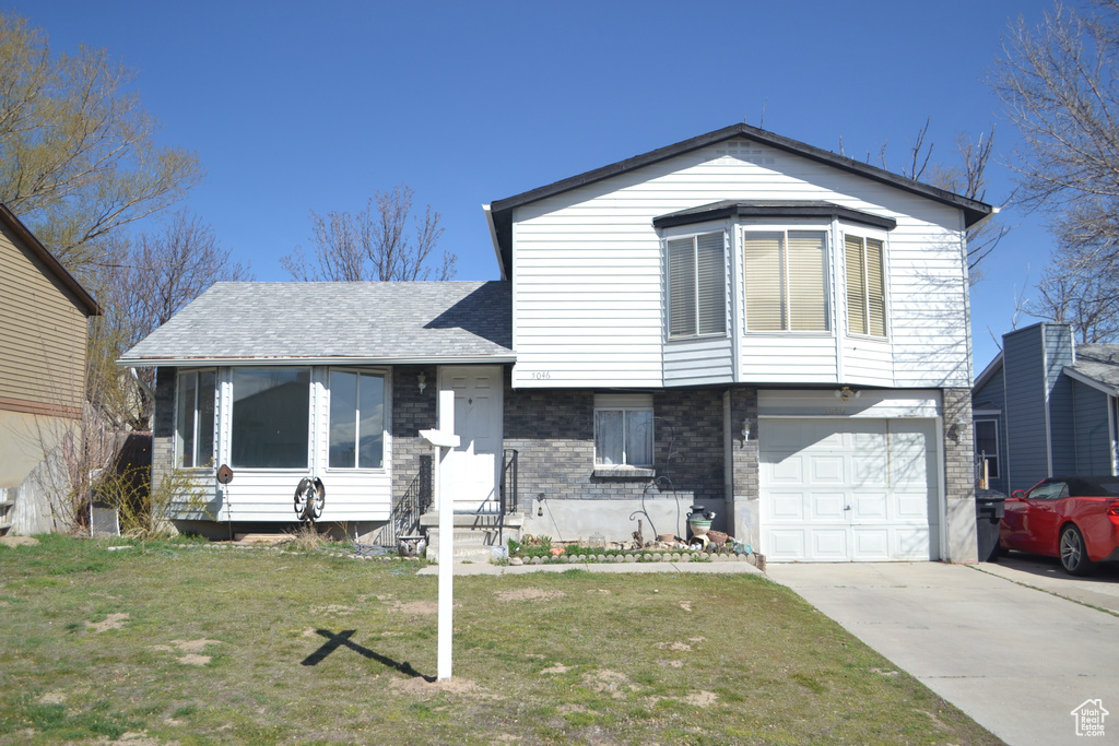 Split level home with roof with shingles, a front yard, an attached garage, and concrete driveway
