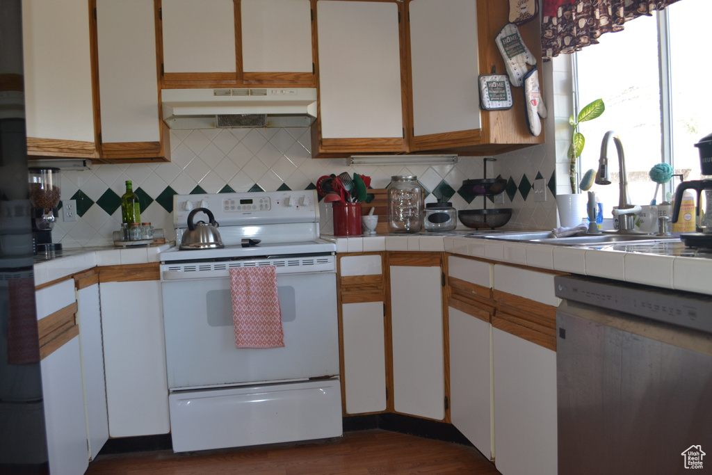 Kitchen featuring a sink, tile counters, dishwasher, white electric range oven, and under cabinet range hood