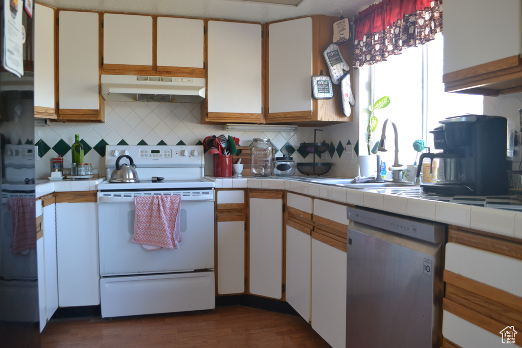 Kitchen with tile counters, dishwasher, under cabinet range hood, electric stove, and a sink