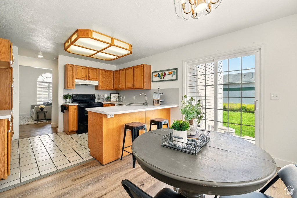 Kitchen with electric range, under cabinet range hood, a peninsula, light countertops, and a chandelier