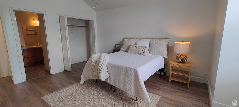 Bedroom with wood finished floors, lofted ceiling, a closet, ensuite bathroom, and baseboards