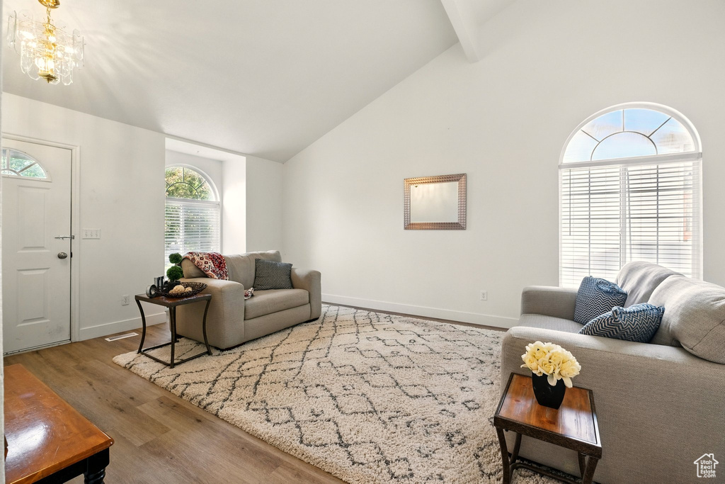 Living area featuring wood finished floors, baseboards, high vaulted ceiling, a chandelier, and beamed ceiling