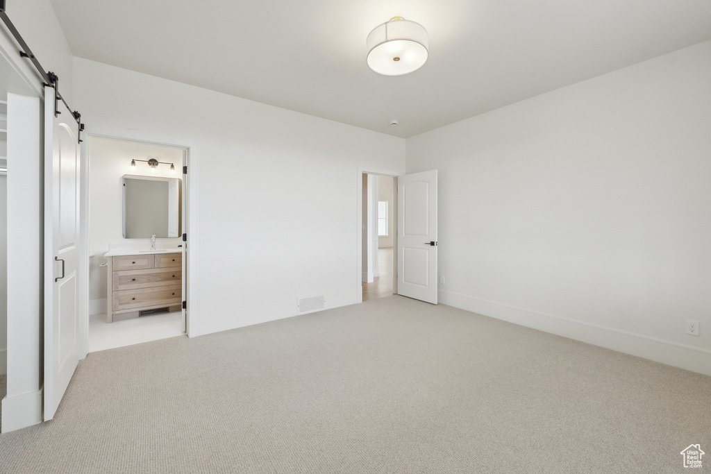 Unfurnished bedroom with a sink, a barn door, baseboards, light colored carpet, and visible vents