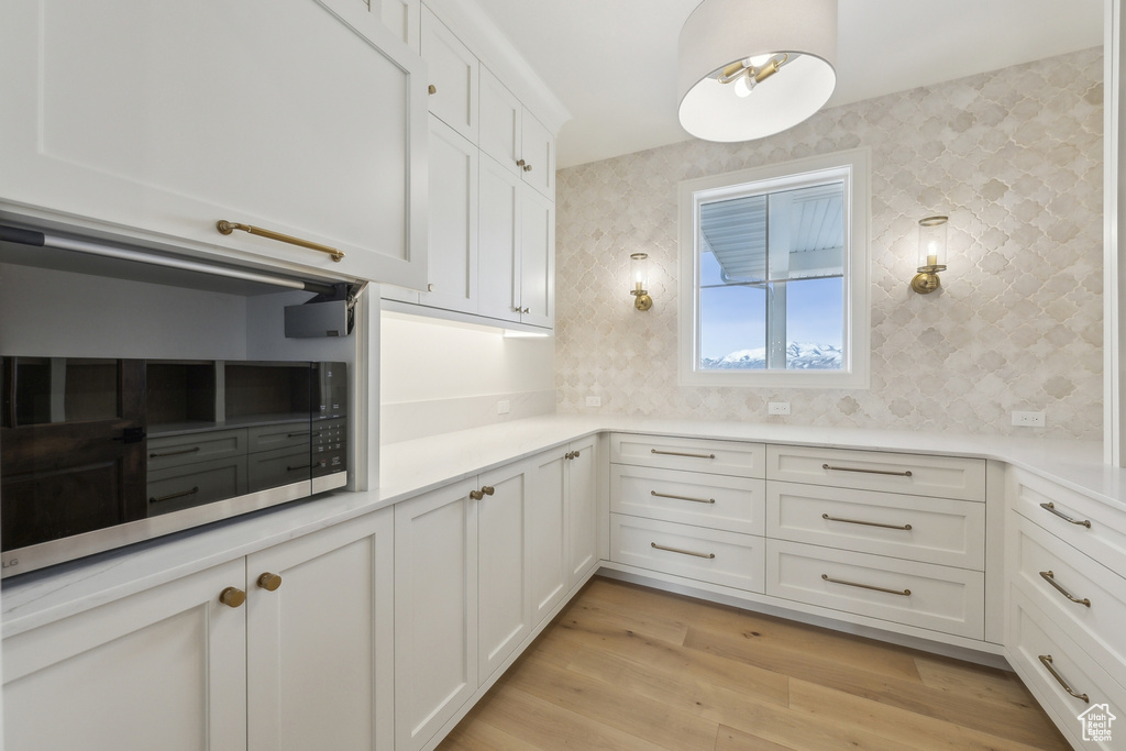 Kitchen featuring light countertops, tasteful backsplash, stainless steel microwave, light wood finished floors, and white cabinets