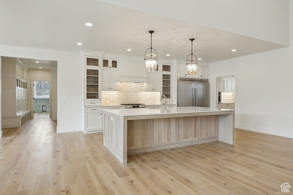 Kitchen with decorative backsplash, light countertops, light wood-type flooring, stainless steel built in fridge, and a large island with sink