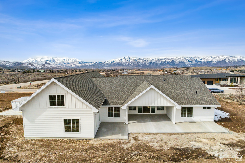 Rear view of property with a shingled roof, a mountain view, board and batten siding, and a patio area