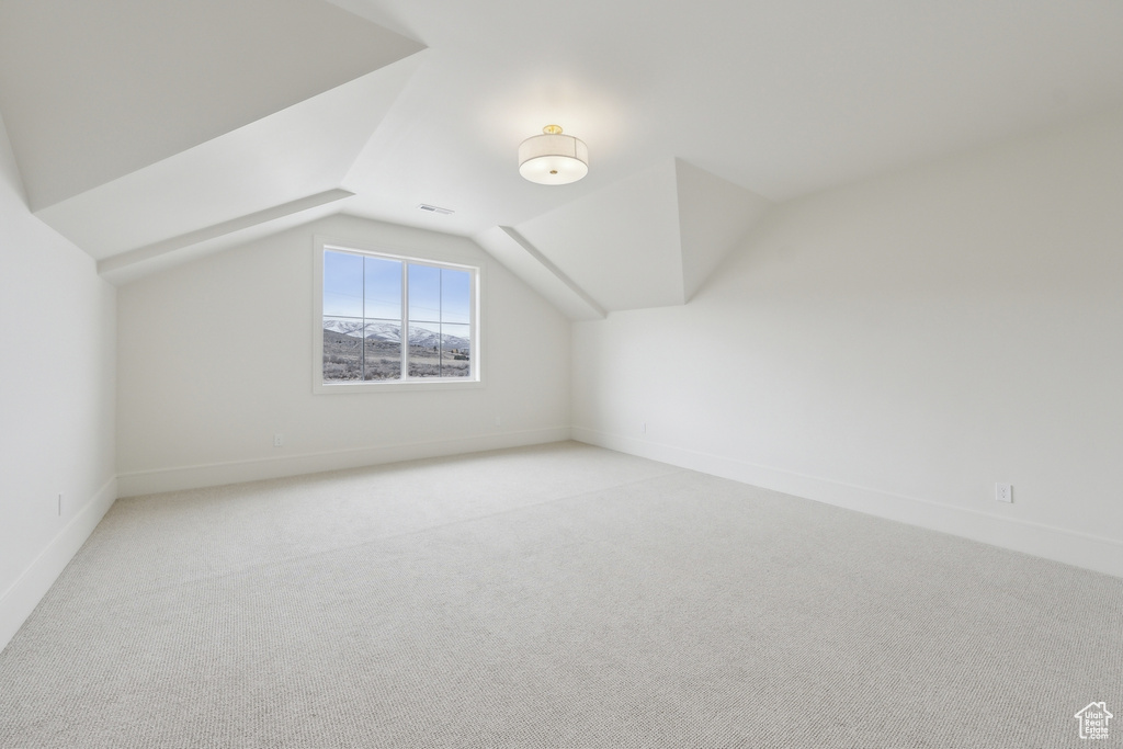 Additional living space featuring light carpet, baseboards, vaulted ceiling, and visible vents