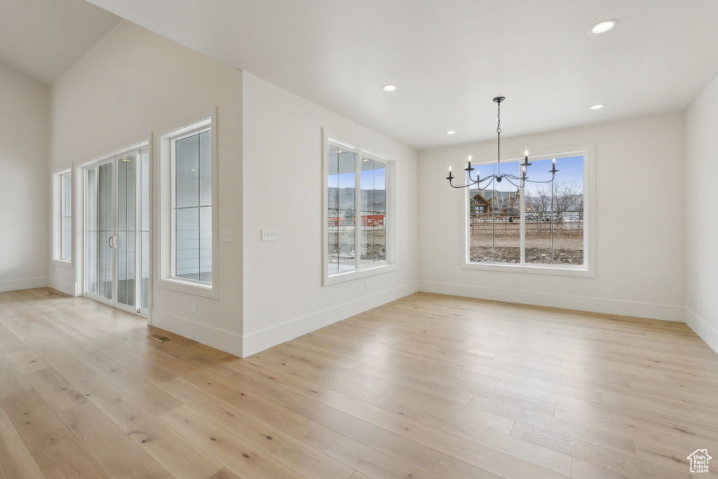 Unfurnished dining area featuring baseboards, a wealth of natural light, light wood-style flooring, and an inviting chandelier