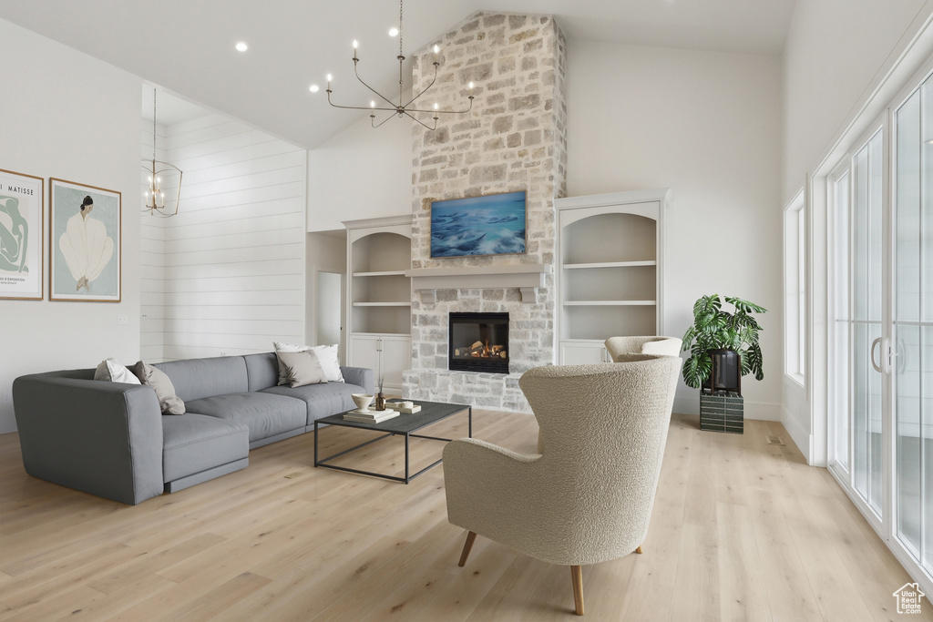 Living area with high vaulted ceiling, an inviting chandelier, light wood-style floors, and a stone fireplace