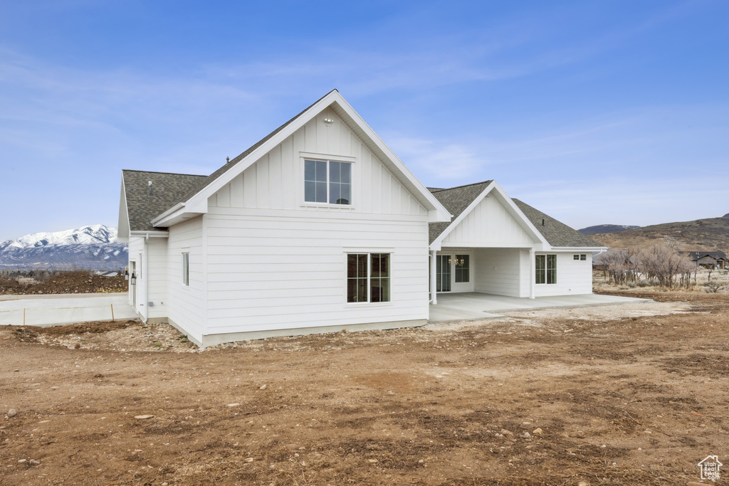 Rear view of house with a mountain view, a patio area, board and batten siding, and roof with shingles
