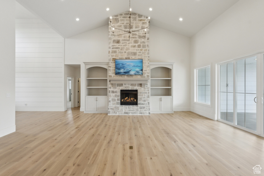 Unfurnished living room with a fireplace, high vaulted ceiling, built in features, and light wood-type flooring
