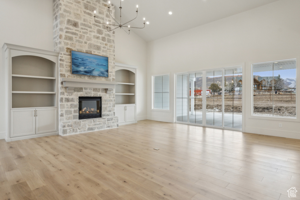 Unfurnished living room with a notable chandelier, high vaulted ceiling, wood finished floors, and a fireplace