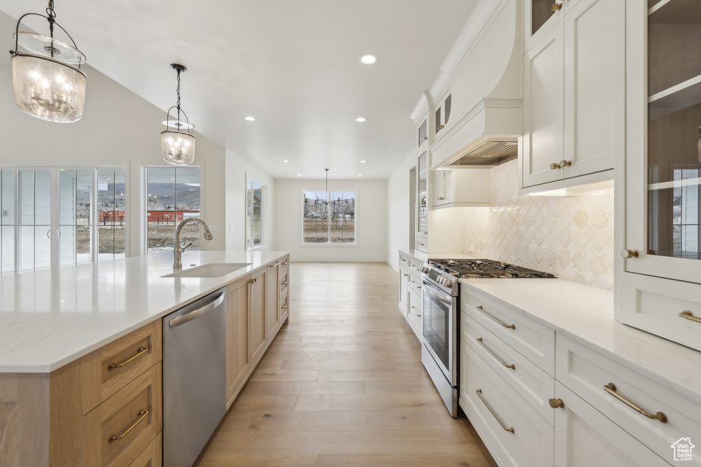 Kitchen with light wood-type flooring, a spacious island, backsplash, a sink, and appliances with stainless steel finishes
