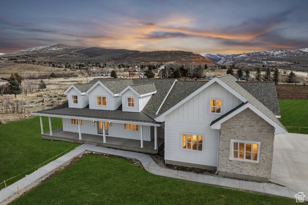 View of front of property featuring stone siding, board and batten siding, a mountain view, a porch, and a yard