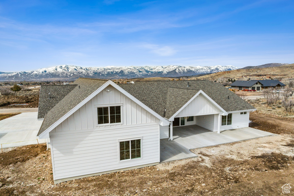 Rear view of property with board and batten siding, a patio, a mountain view, and a shingled roof