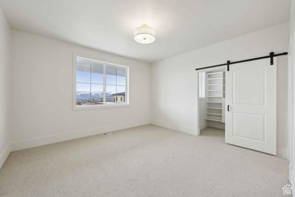 Unfurnished bedroom featuring light carpet, baseboards, a closet, and a barn door