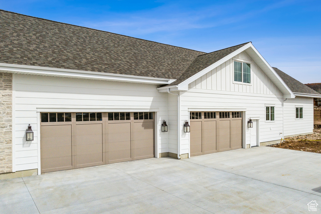View of side of property with roof with shingles, an attached garage, board and batten siding, and concrete driveway