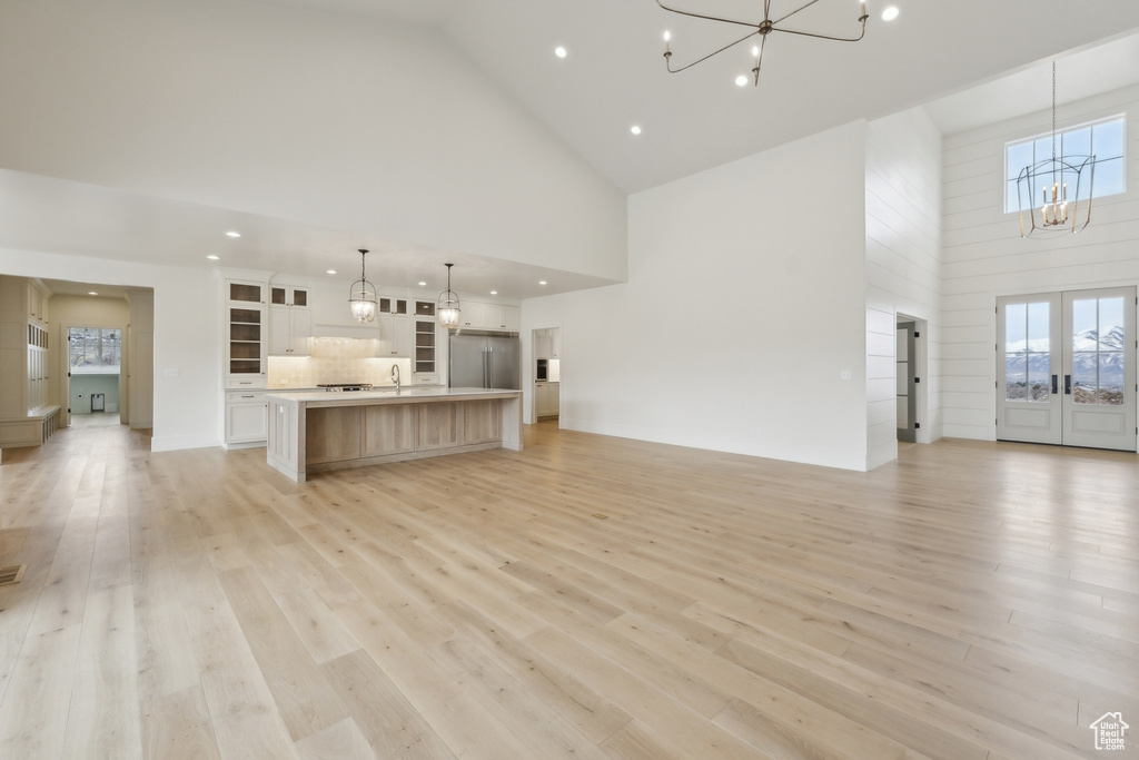 Unfurnished living room featuring french doors, high vaulted ceiling, a sink, light wood-style floors, and a notable chandelier