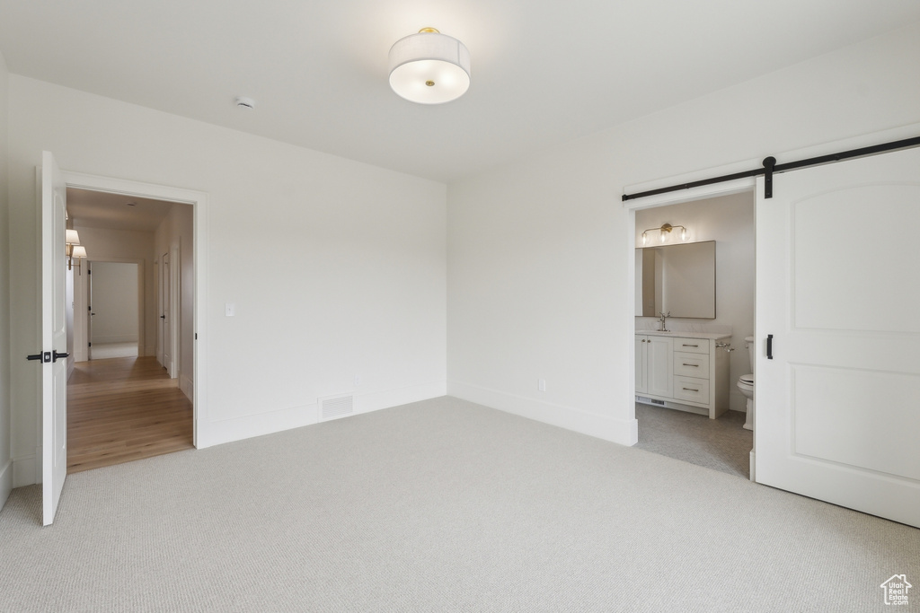 Unfurnished bedroom with light carpet, a barn door, ensuite bathroom, and visible vents