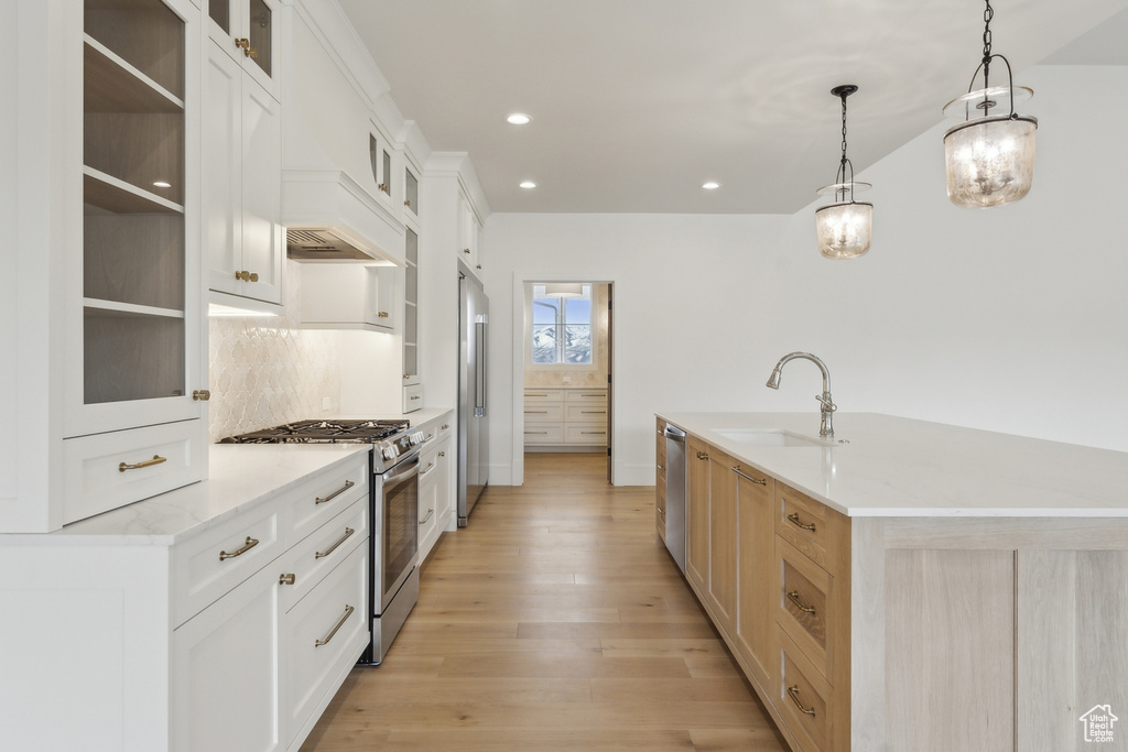 Kitchen with backsplash, a sink, light wood-style flooring, stainless steel appliances, and recessed lighting