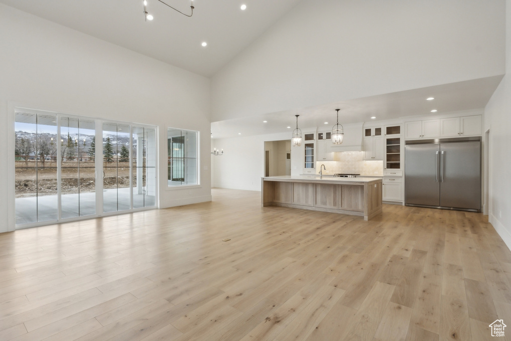 Unfurnished living room featuring high vaulted ceiling, recessed lighting, a notable chandelier, and light wood finished floors