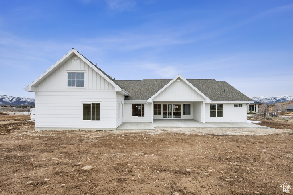 Rear view of house featuring a mountain view, a patio, board and batten siding, and roof with shingles