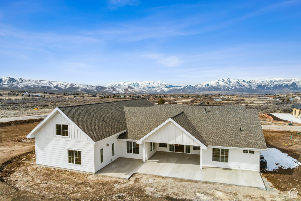 View of front of property with board and batten siding, a mountain view, roof with shingles, and a patio area