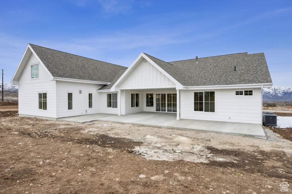 Rear view of house featuring a patio, central air condition unit, board and batten siding, and roof with shingles