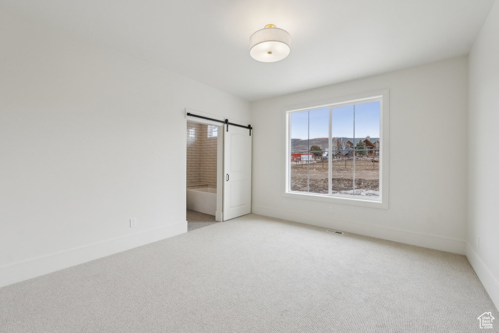Unfurnished room featuring light colored carpet, visible vents, a barn door, and baseboards