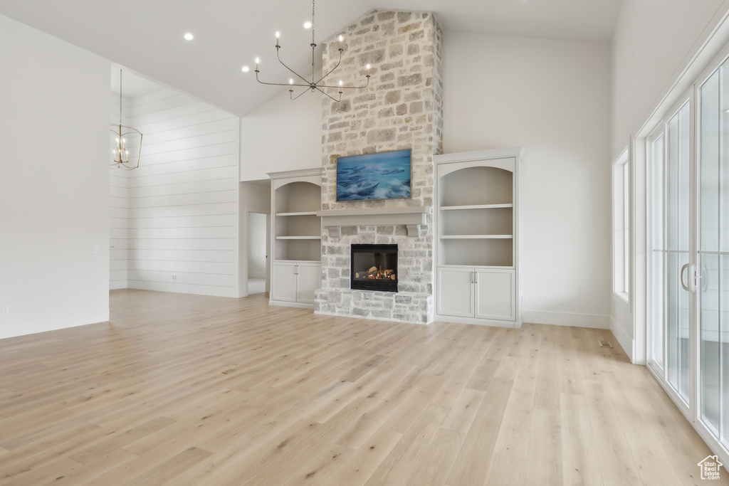 Unfurnished living room with high vaulted ceiling, baseboards, a stone fireplace, light wood-type flooring, and an inviting chandelier