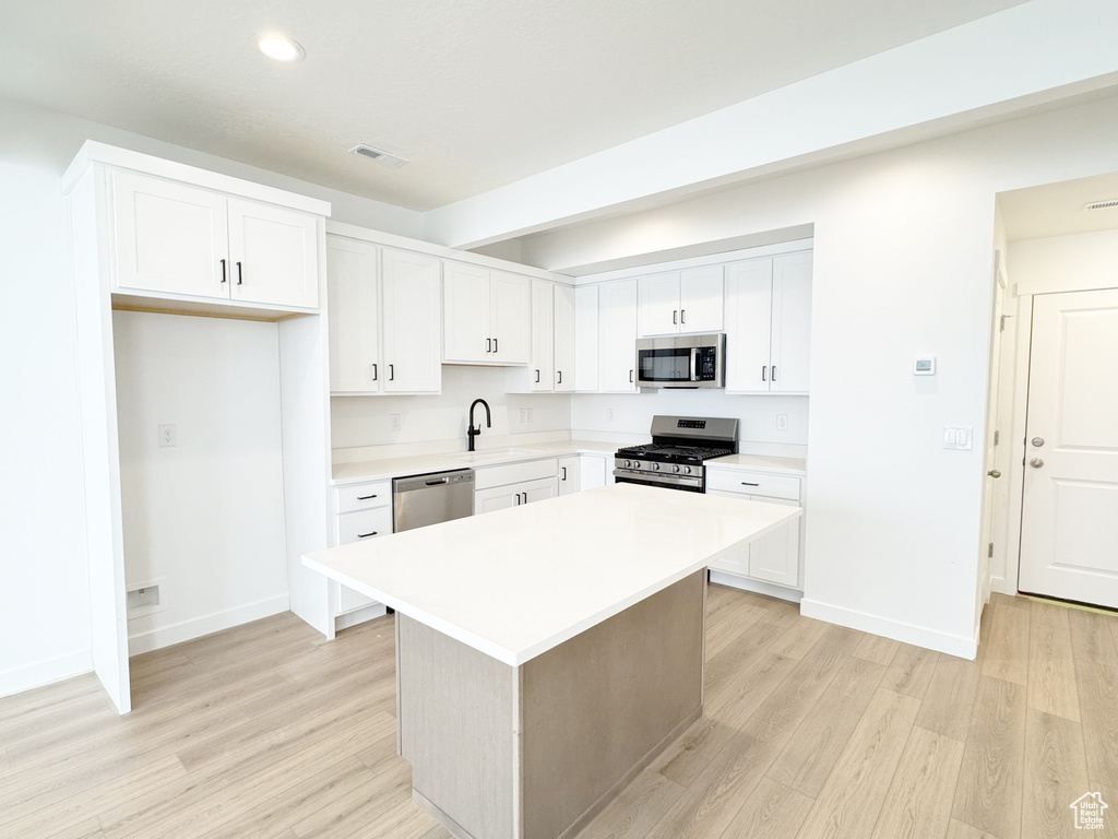 Kitchen featuring light countertops, a sink, stainless steel appliances, baseboards, and light wood-style floors