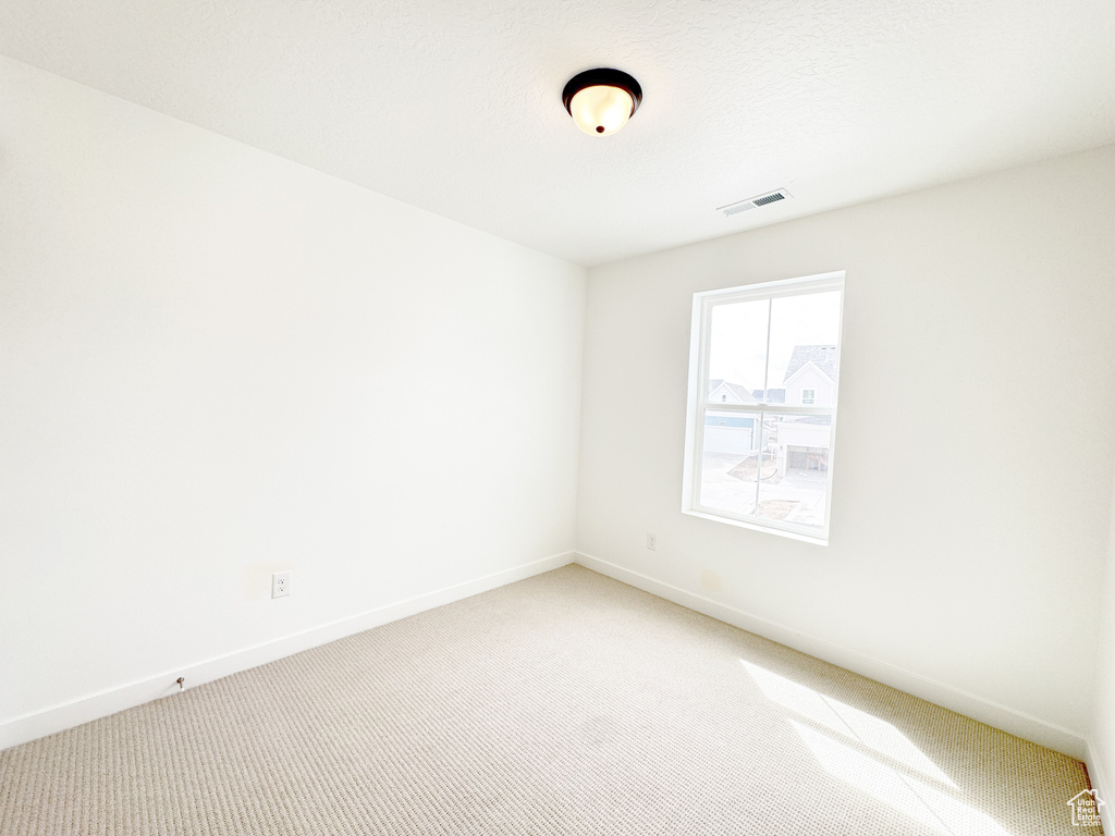 Spare room featuring baseboards, visible vents, and light colored carpet